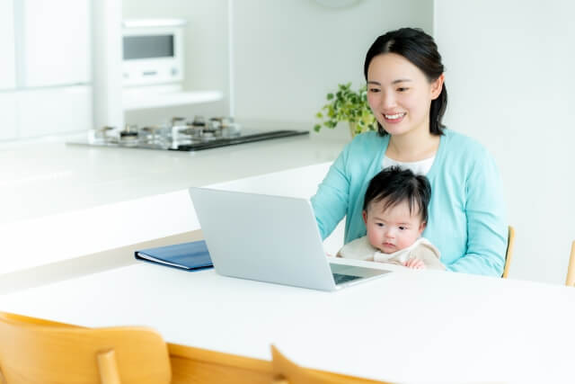 子供を抱っこしながらパソコンをするママ